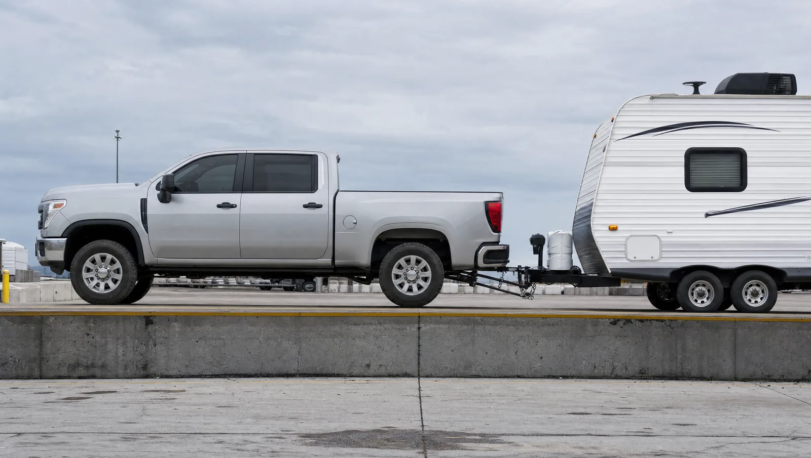 Side view of a pickup truck hitched to a travel trailer on a weigh scale platform, with the front axle, rear axle and the trailer's tandem axles all visible in a row.