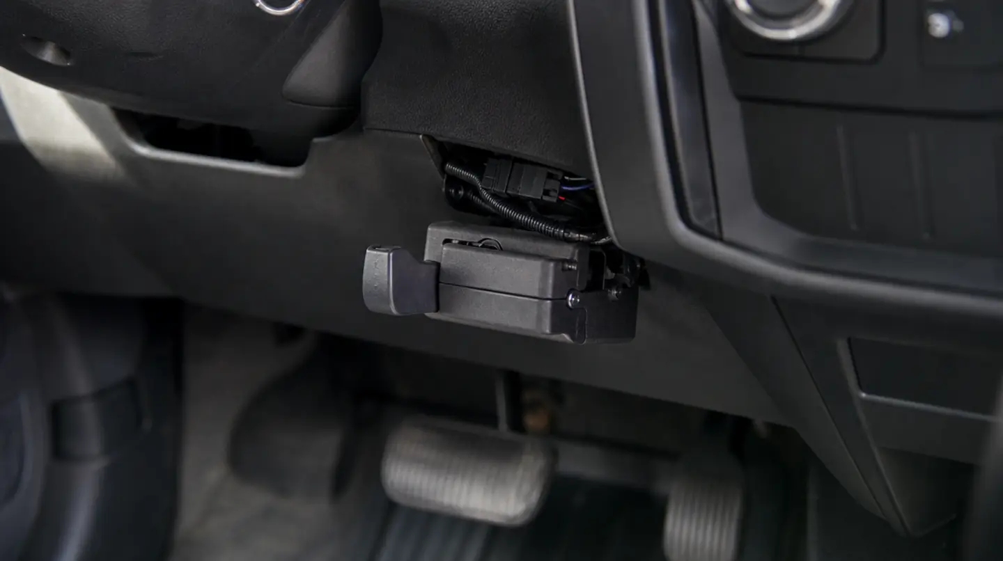 A trailer brake controller mounted below the steering column of a pickup truck, showing its manual override lever and the wiring harness behind.