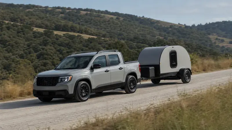A compact pickup towing a teardrop camper on a country road