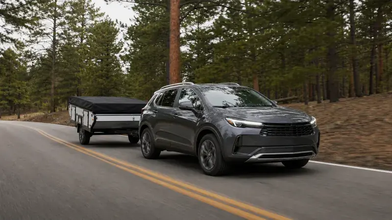 A compact crossover towing a pop-up camper through a forest