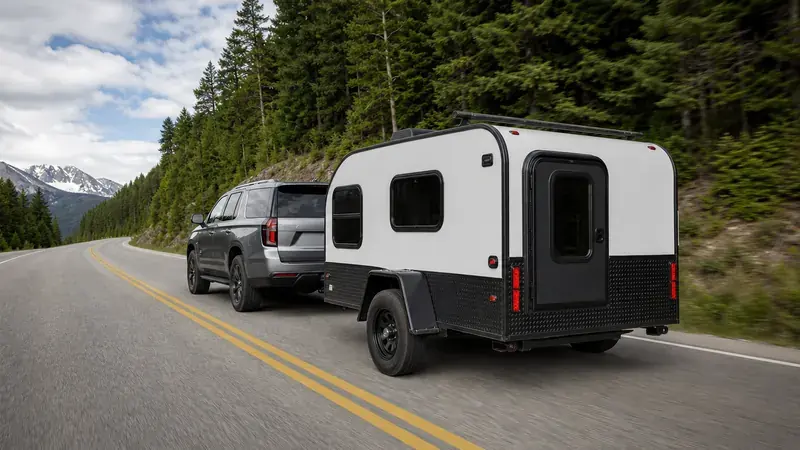 An SUV towing a small camper on a mountain road