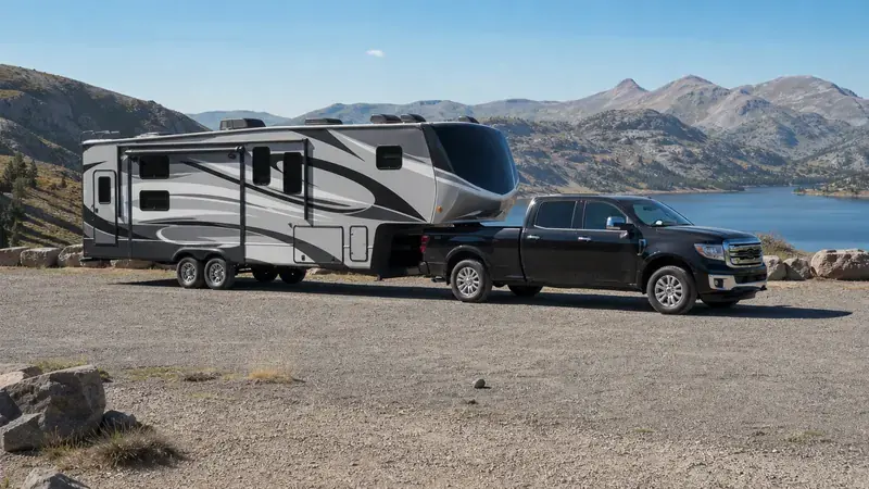 A pickup towing a fifth-wheel trailer beside a mountain lake